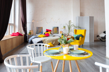 Trendy fashion luxury interior design in Scandinavian style of studio apartment with bright yellow furniture and decorated with new year lights.