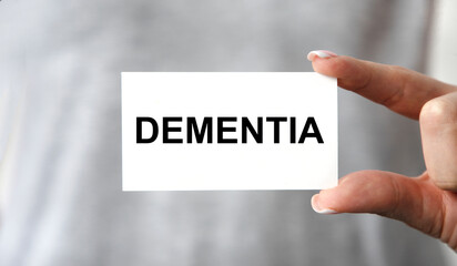 The girl holds a card with the text OF DEMENTIA, the background is gray.