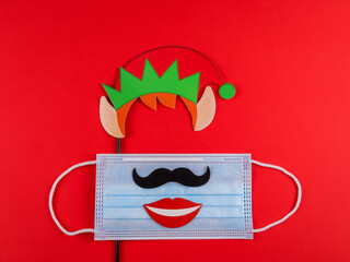 Mask, smile, mustache and santa hat lie in the middle on a red background, close-up top view.