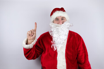 Man dressed as Santa Claus standing over isolated white background showing and pointing up with fingers number one while smiling confident and happy