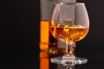 Glass of whisky with ice on black background