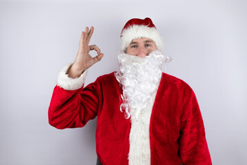 Fototapeta na wymiar Man dressed as Santa Claus standing over isolated white background doing ok sign with fingers and smiling, excellent symbol