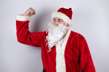 Fototapeta na wymiar Man dressed as Santa Claus standing over isolated white background showing arms muscles smiling proud