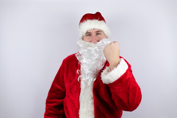 Fototapeta na wymiar Man dressed as Santa Claus standing over isolated white background angry and mad raising fist frustrated and furious while shouting with anger. Rage and aggressive concept.