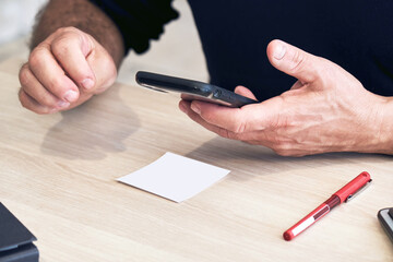 Businessman holds a mobile phone or smartphone in his hand on a wooden office table