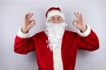Fototapeta na wymiar Man dressed as Santa Claus standing over isolated white background relax and smiling with eyes closed doing meditation gesture with fingers