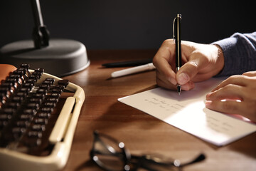 Man writing letter at wooden table indoors, closeup