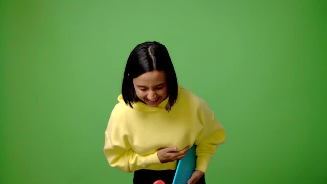 Young skater woman on green screen chroma key background smiling a lot while covering mouth