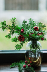 Christmas composition with spruce branches, artificial flowers and berries in a vase against the background of a window.