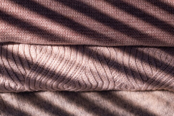 Stack of pastel color winter knitted sweaters background with shadow. Cozy Autumn and winter concept close up image.