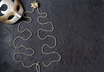Carnival mask with gold decoration in the form of a Christmas tree on a black background. Place for signature.