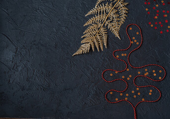 Golden artificial branch, red ornaments in the form of a Christmas tree and gold stars on a black background.