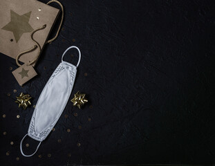 Protective medical mask, gold sequins, gift bag on a black background. Christmas composition..Place for signature.