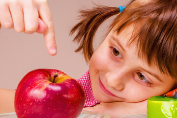 Close up portrait of cute young girl having hard choice between healthy and unhealthy food. She choosing between apple fruit and tasty cake.