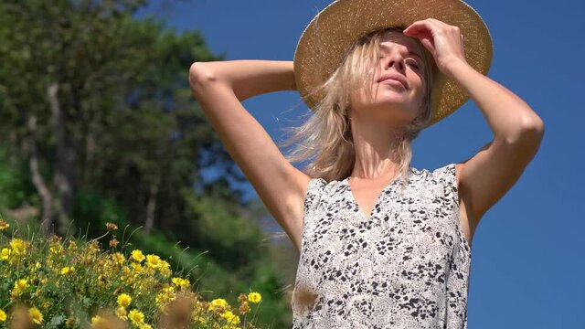 blonde with straw hat posing while wind blowing in the field