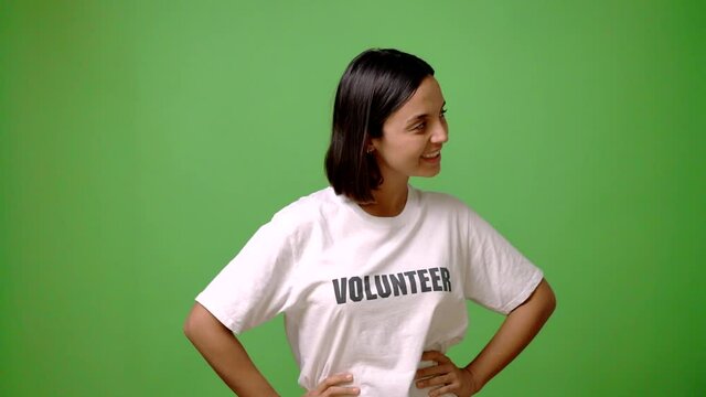 Young volunteer woman on green screen chroma key background posing with arms at hip and laughing