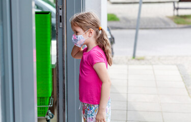 Obraz na płótnie Canvas Little girl, school age child in protective anti viral face mask entering a shop, convenience store alone, on her own. Children and shopping during covid 19, corona virus pandemic concept, protection