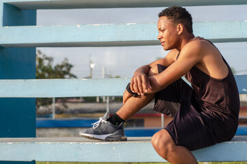young dark-skinned latino man sitting on the stairs with a good body exercising in the park with...