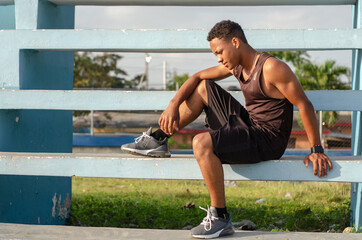 young dark-skinned latino man sitting on the stairs with a good body exercising in the park with...