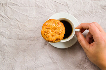 A hand holding a cup of black espresso coffee and cooky on the white cloth background