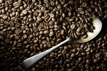 Roasted coffee beans flat lay with a steel spoon in dramatic side light. Top view with copy space. Stock - 396360142