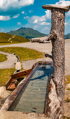 Beautiful alpine summer view with a wooden water well at the famous Panoramabahn Kitzbueheler Alpen, Salzburg, Austria