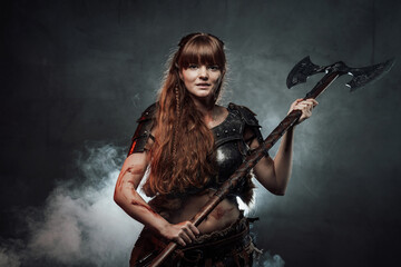 Wielding axe smiley woman viking dressed in dark light armour with brown hairs poses in dark foggy...