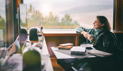 Young woman in a green sweater drinking coffee sitting by the window in a country house with mountain view