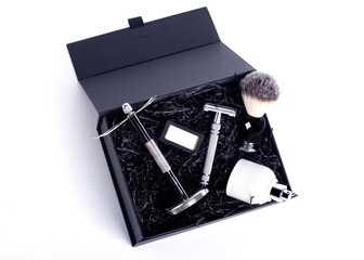 Razor and brush on stand, perfume, balsam and blades in black box on a white background.
