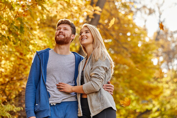 sportive married couple have leisure adventure time in the forest, stand in contemplation, looking up at yellow trees. at sunny autumn day