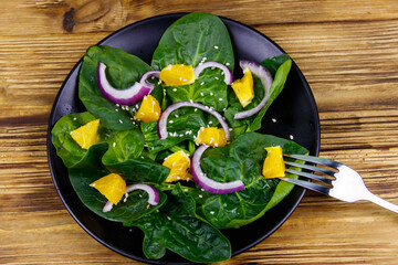 Tasty salad with spinach, orange, red onion and sesame seeds on wooden table. Top view. Healthy food or vegetarian concept