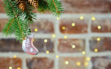 Festive Christmas card with a branch of a Christmas tree with a toy on the background of a brick wall decorated with a garland, selective focus. Christmas template for banner or postcard, close-up