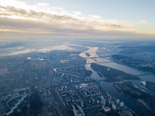 Fototapeta premium Aerial high flight over Kiev, haze over the city. Autumn morning, the Dnieper River is visible on the horizon.