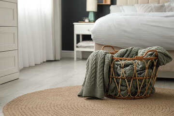 Knitted green plaid in wicker basket near bed indoors, space for text