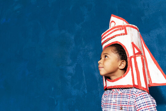 Afro-american kid boy with craft rocket on head. Close up side view of cute little child with spaceship, portrait with copyspace for advertising text. Space learning and education concept.