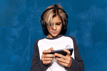 Portrait of school boy in headphones using smartphone application, studying or playing. Teen in...