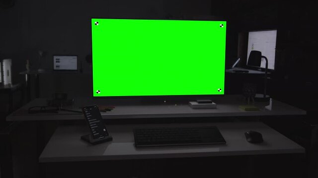 Remote working. Home office setup. Green screen desktop computer on dark room. Several devices in the background.  Chroma key. Put your own images or videos. Track corners with perspective corner pin.