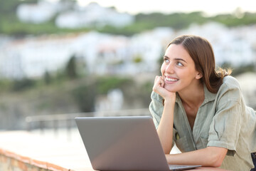 Tourist dreaming with a laptop looking at side in a balcony