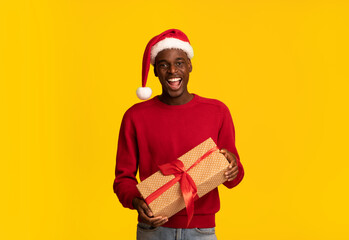 Enjoying Holidays. Cheerful Black Man In Santa Hat Holding Christmas Present Box