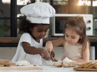 Two cute little diversiy girls enjoy and help each other baking. Diverse and Education concept.
