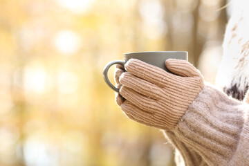 Woman hands with gloves holding coffee mug in autumn