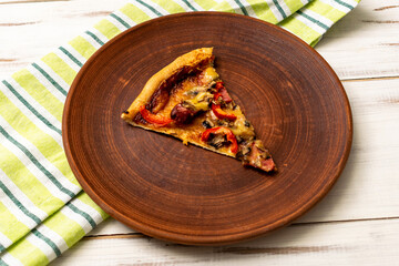 A piece of pizza on a plate on a wooden background.