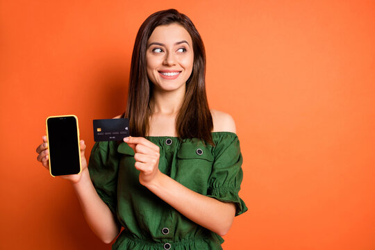 Photo of lady wear green off-shoulders blouse holding bank card modern device looking empty space isolated orange color background