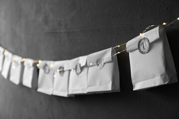 Paper bags hanging on black wall, closeup. Christmas advent calendar