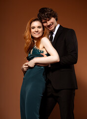 Beautiful red long hair style woman and handsome man with joyful smle celebrating new year holiday in fashion elegant clothes on orange bright background. Closeup