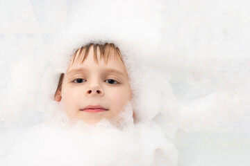 A boy in soapy suds is washing in a bath. Hygiene, cleanliness concept.