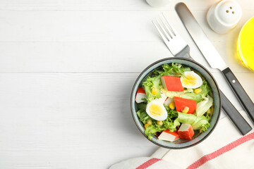 Delicious salad with crab sticks and eggs in bowl on white wooden table, flat lay. Space for text