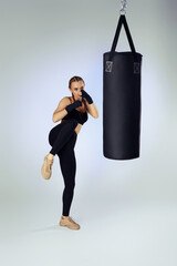 sporty fit woman with boxing bandages in sportswear hitting making kick during boxing exercise on studio background