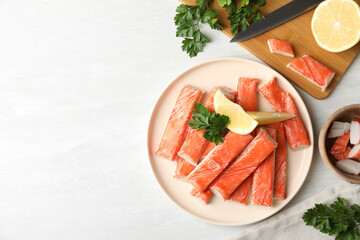 Flat lay composition with crab sticks and lemon on white table, space for text