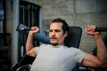 Determined and focused young Hispanic man doing chest exercises on a machine in modern gym. Healthy and active sport lifestyle